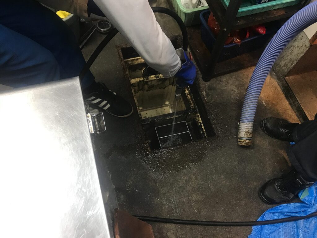 グリストラップを清掃中。脂というよりは、炭や焦げのゴミが大量に溜まっています。